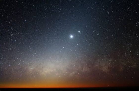 Venus shining brightly above the horizon in a star-filled night sky, with the Milky Way and an orange twilight glow below
